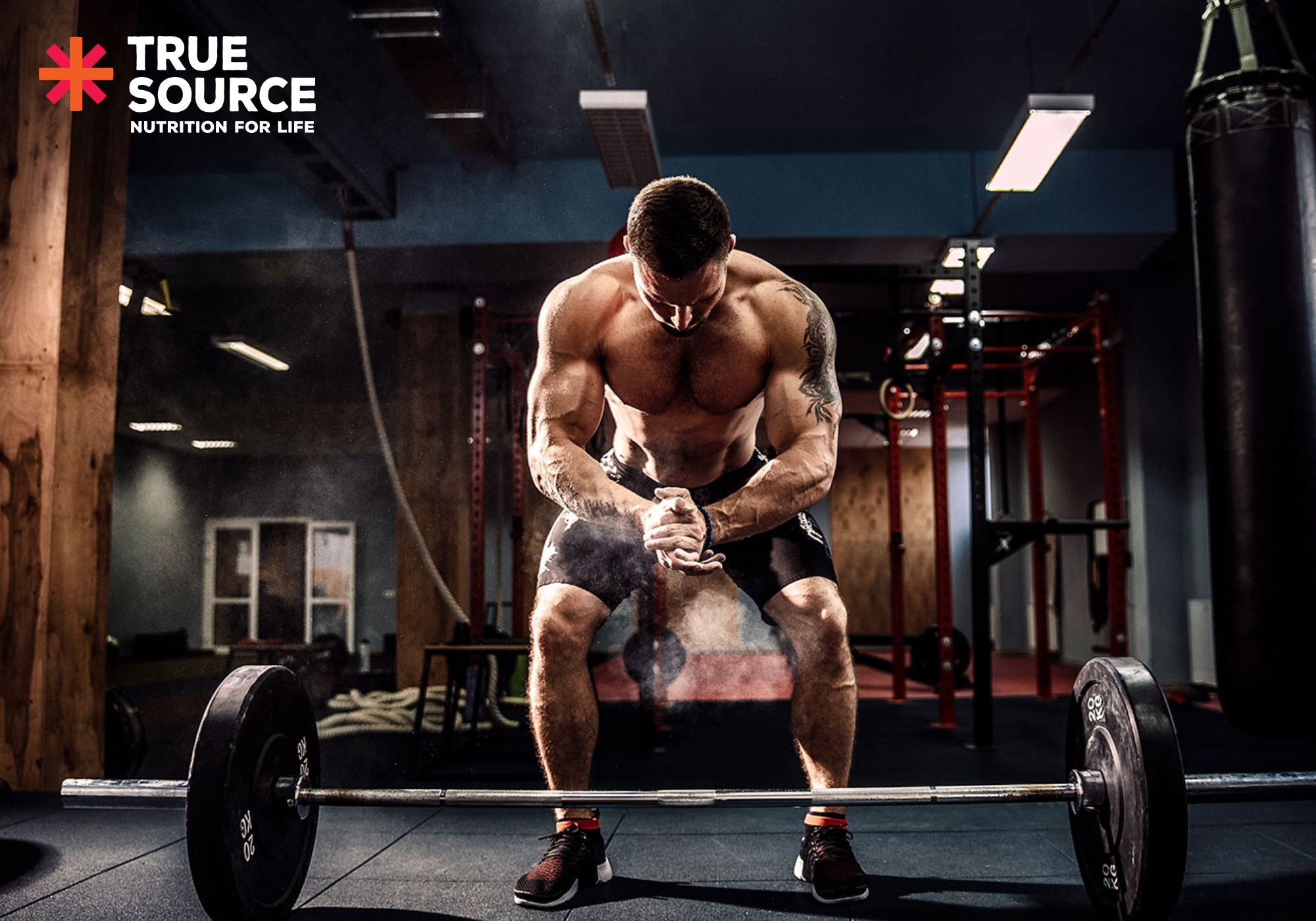 homem em um fundo de academia agachado em frente a um peso de musculação