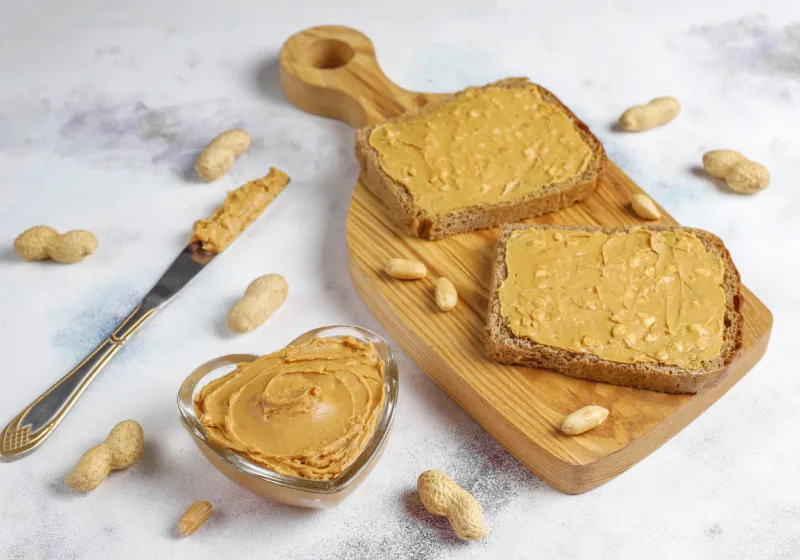 torrada integral com pasta de amendoim sanduíches de manteiga de amendoim em cima da tabua de madeira com um pode em formato de coração com manteiga de amendoim com uma faca do lado