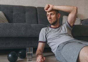 homem encostado no sofá com peso de academia e água