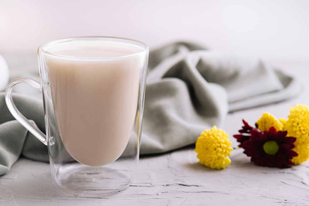 Copo de vidro com bebida cremosa e flores ao fundo