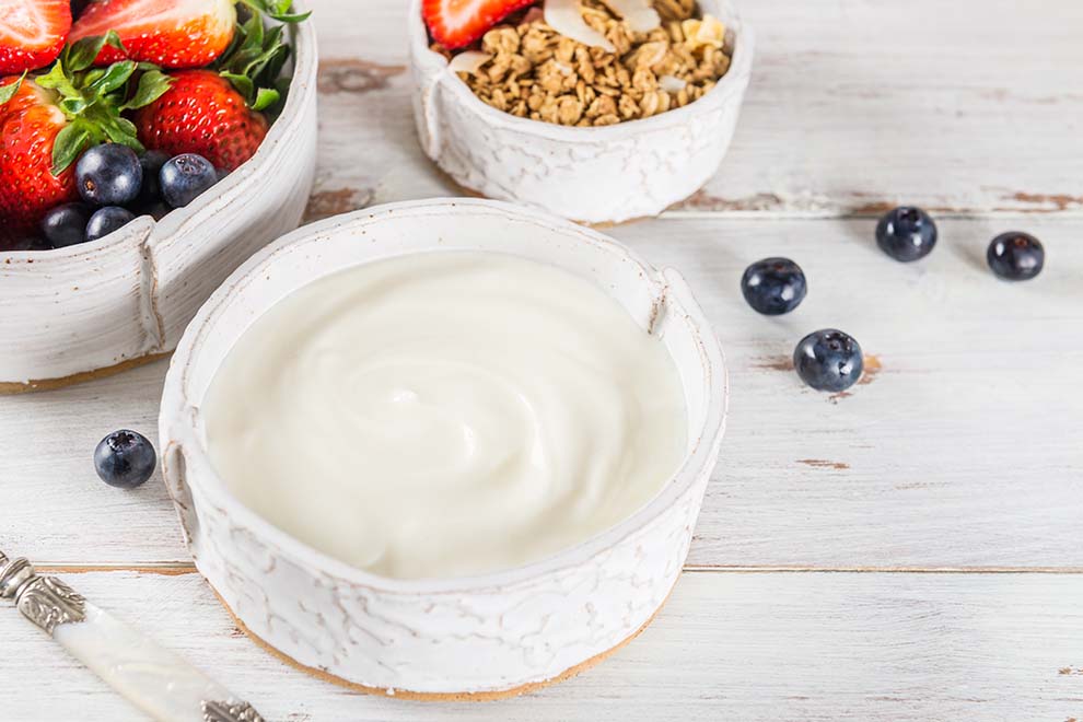 Tigela de iogurte com frutas e granola ao fundo