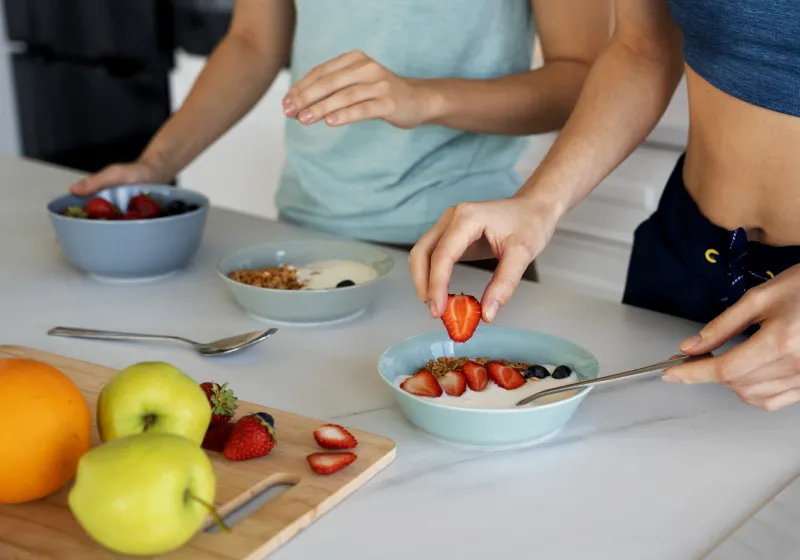mulheres preparando refeições saudáveis com iogurte morango granola maça e uvas de alto ângulo