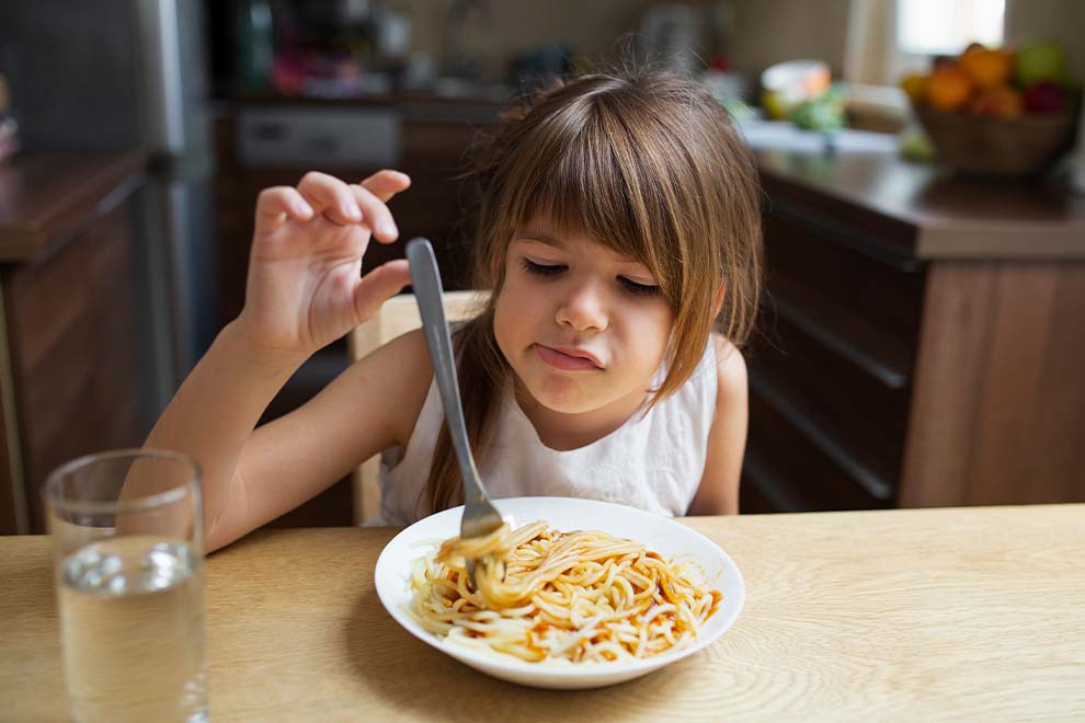 Menina comendo espaguete em mesa de jantar