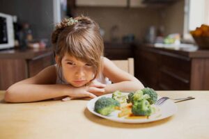 Menina triste ao olhar para brócolis no prato
