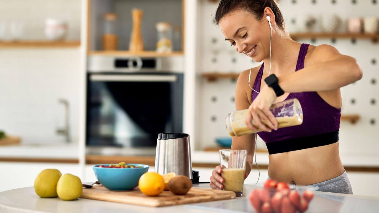 Mulher colocando batida de frutas com whey em um copo.