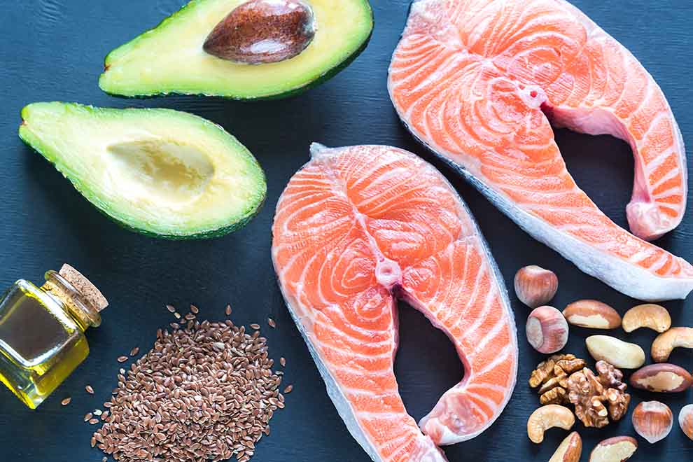 alimentos com ômega 3 vários alimentos ricos em ômega 3, como salmão, abacate, castanhas e azeite em cima de uma mesa escura