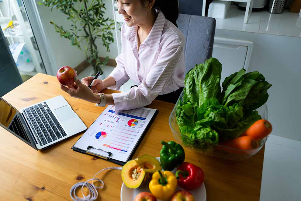 dieta personalizada Mulher analisando gráficos com frutas e verduras na mesa.