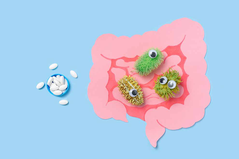 intestino desenhado com pequenos microbiotas feitos em brinquedos e um pequeno pote azul com remédios ao lado em cima de uma mesa azul claro