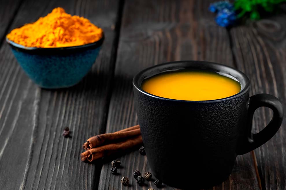 chá de cúrcuma Pó de cúrcuma em tigela de madeira com raízes ao redor.