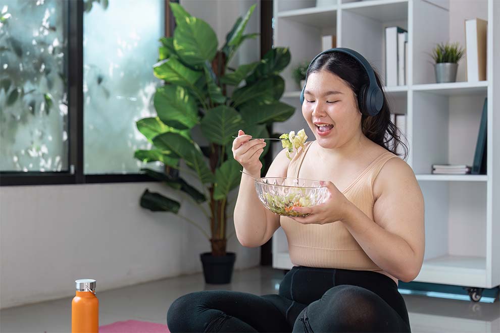 Mulher feliz comendo salada em ambiente relaxante.