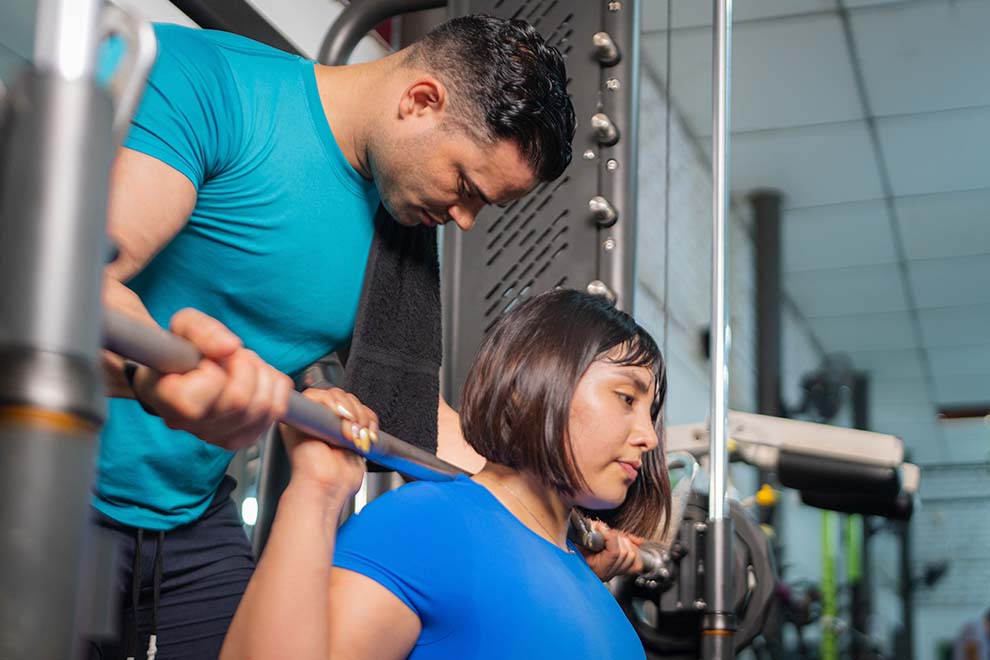 personal ajudando a mulher a fazer musculação em uma academia privada 