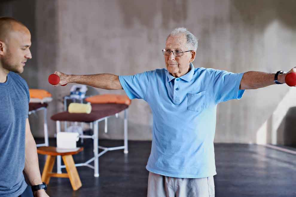 sarcopenia intro Idoso exercitando-se com halteres, supervisão de treinador.