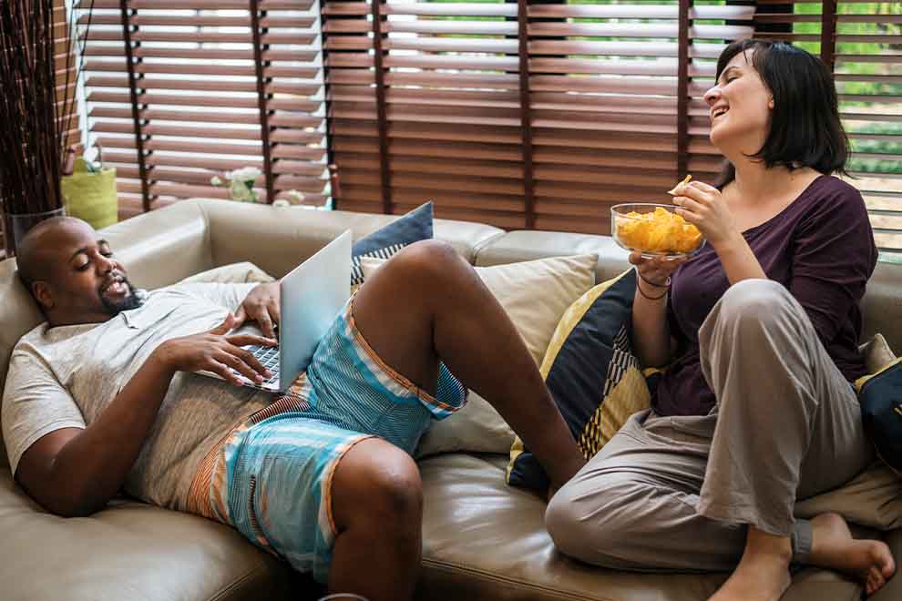 sedentarismo Casal relaxando no sofá com laptop e petiscos