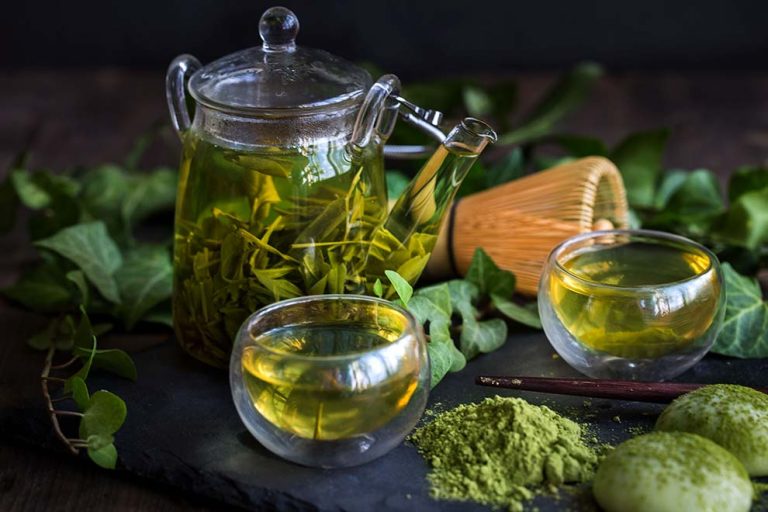 Chá verde em pote com folhas e xícaras