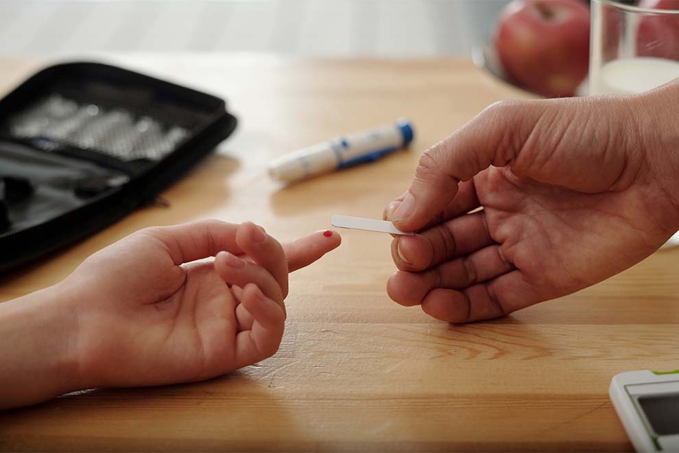 mulher fazendo o teste de diabetes em cima de uma mesa de madeira perto da cozinha