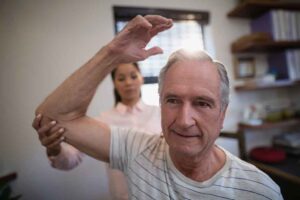 Fisioterapeuta ajudando idoso com exercícios de mobilidade.