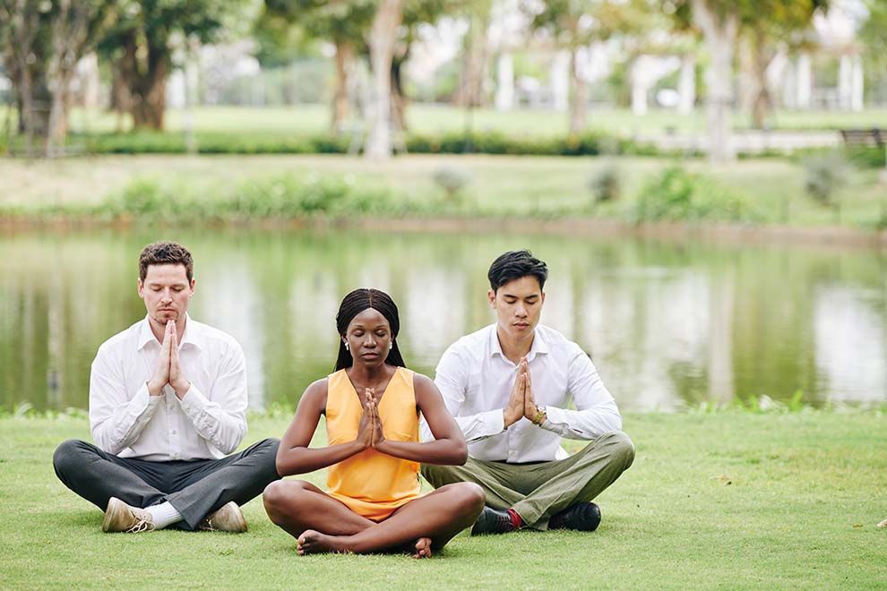 três pessoas fazendo o mindfulness em um parque em um dia ensolarado