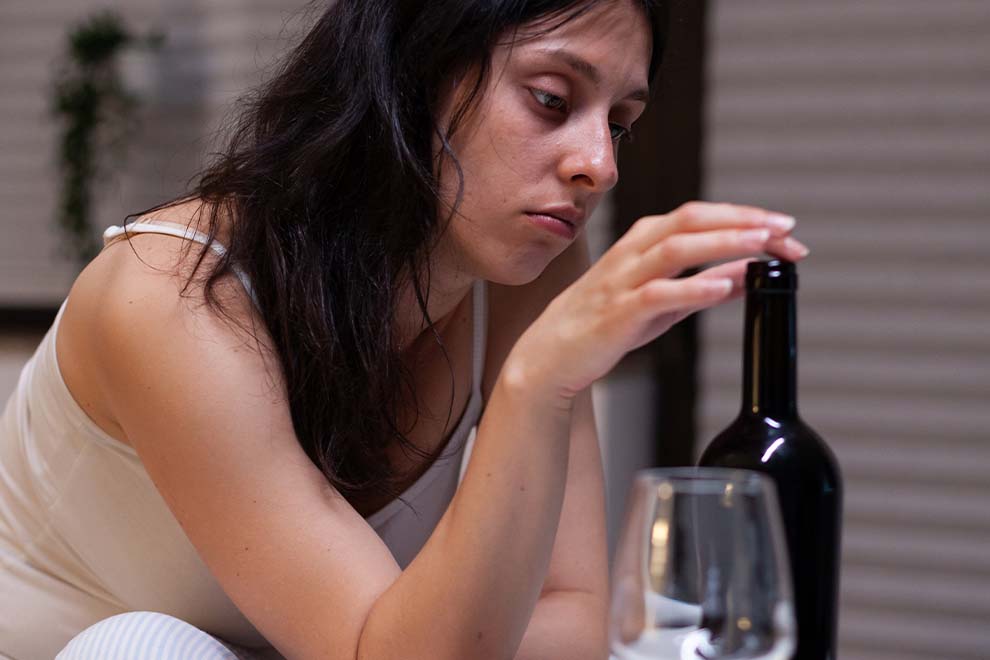 mulher com garrafa de vinho e uma taça a sua frente por beber demais