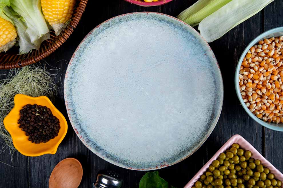 cloreto nos alimentos Prato vazio rodeado de vegetais e grãos variados.