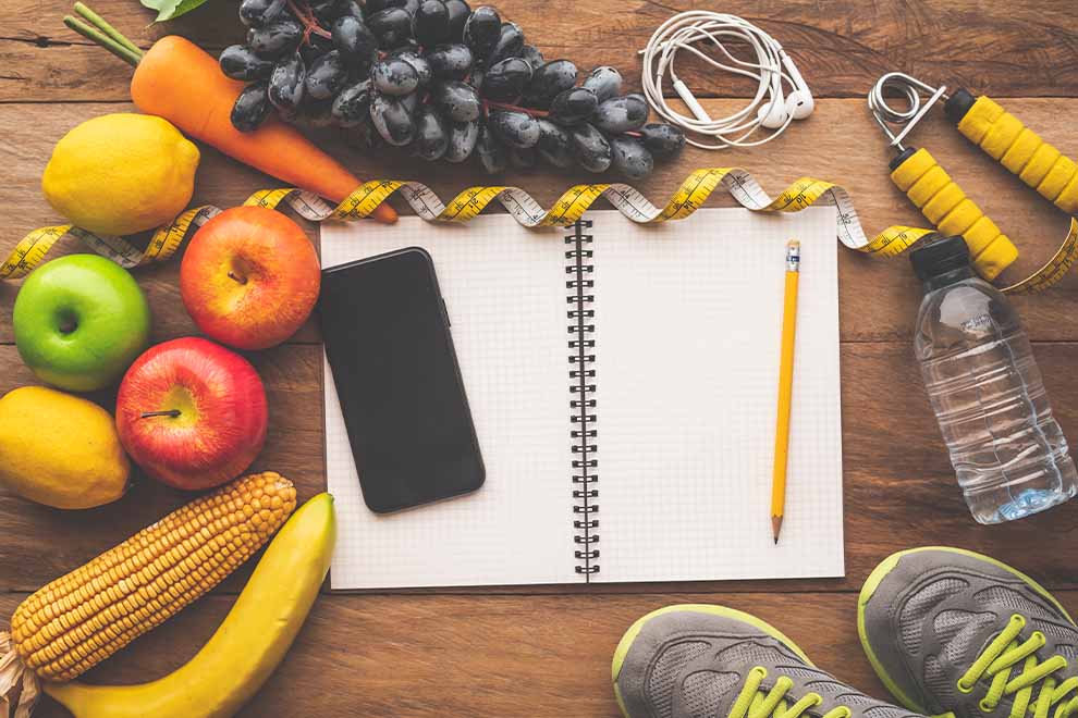 Mesa com frutas, notebook e itens de fitness
