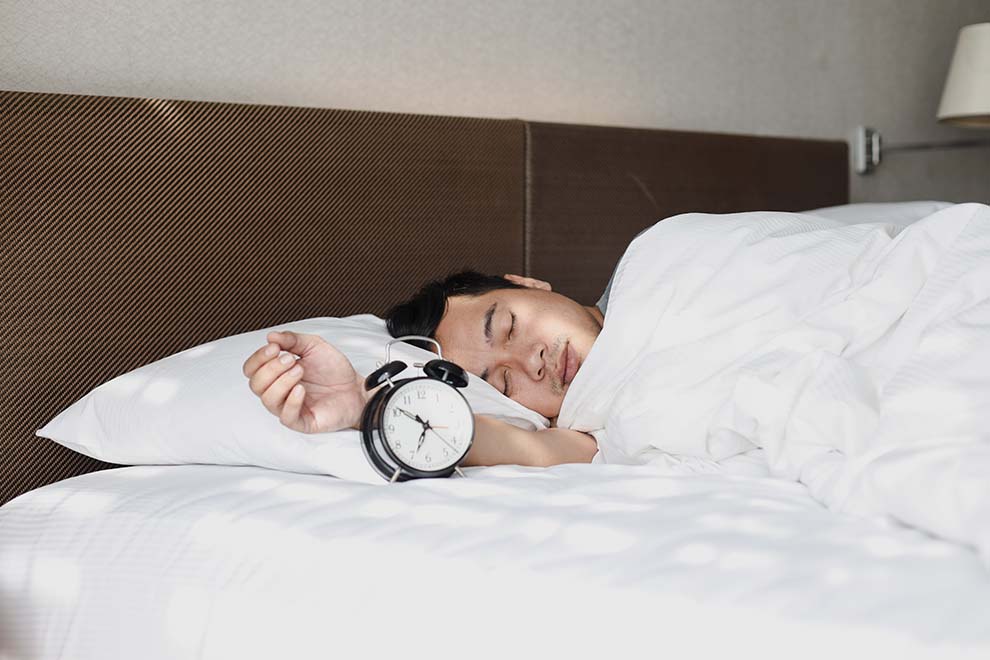 Homem dormindo com despertador ao lado na cama