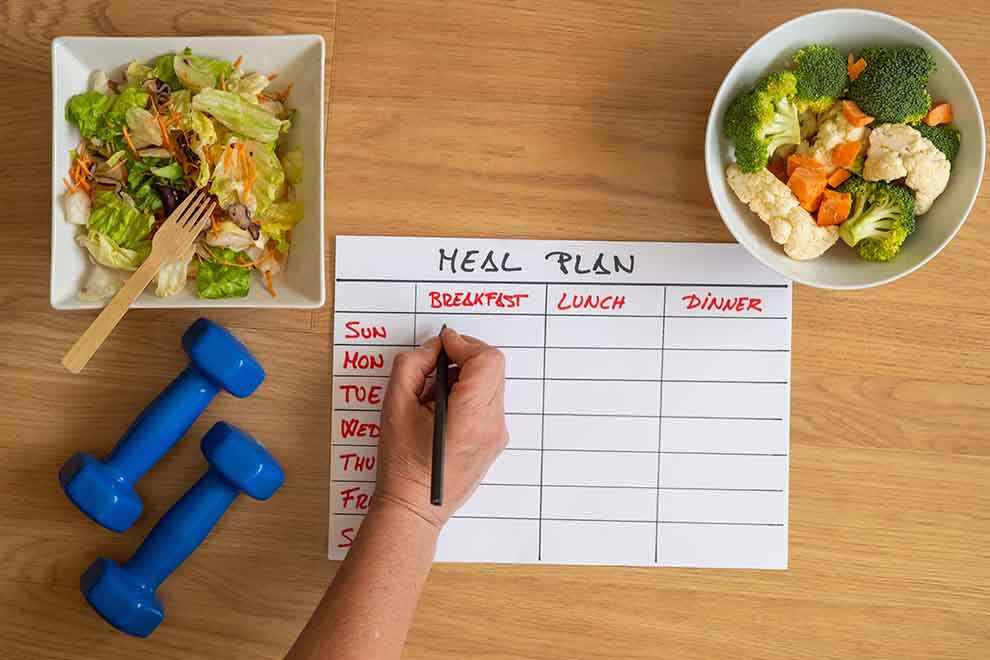 Pessoa escrevendo um plano de refeições com saladas e legumes.